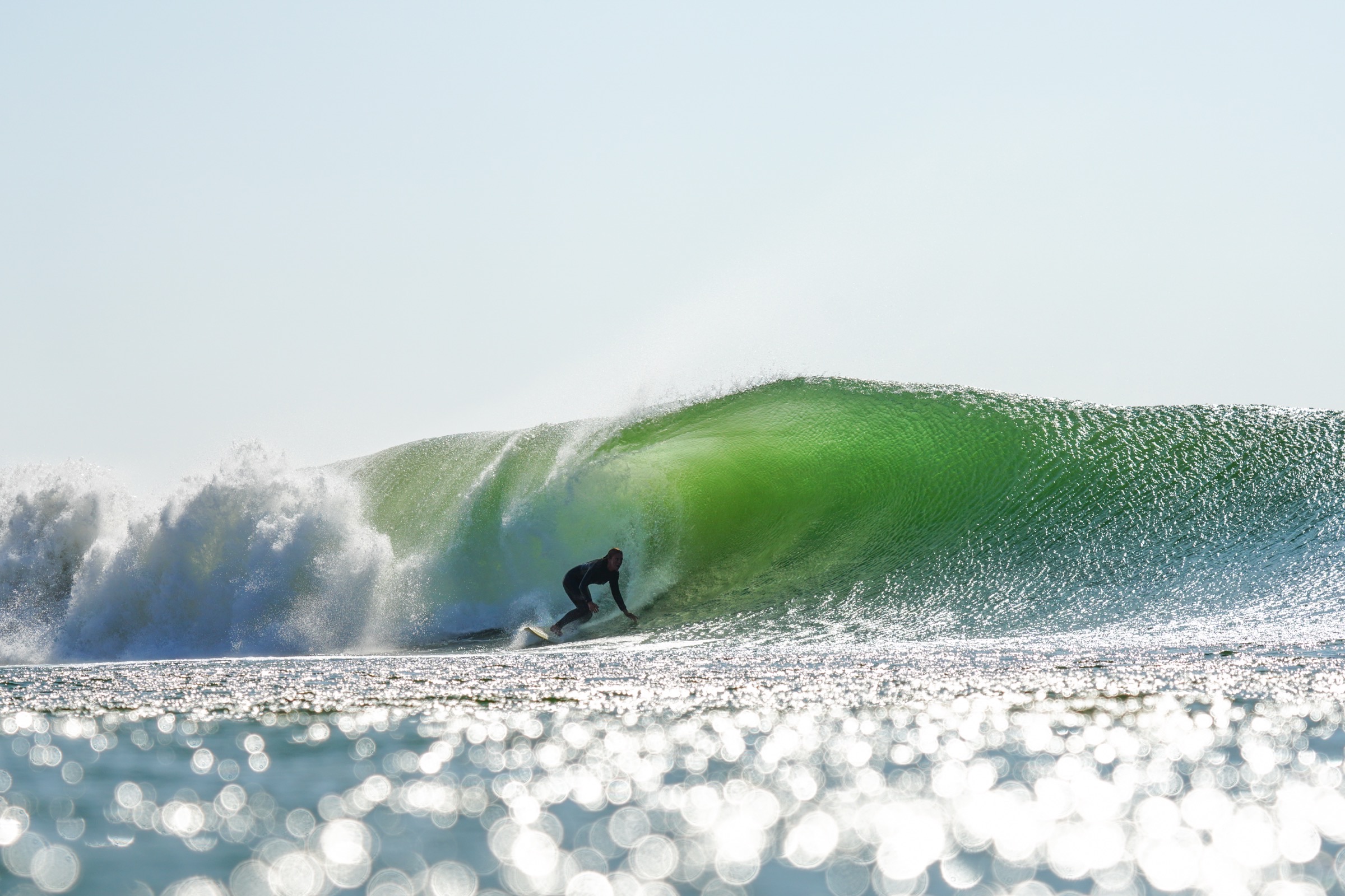 A surfer setting a rail deep inside a bright green barrel