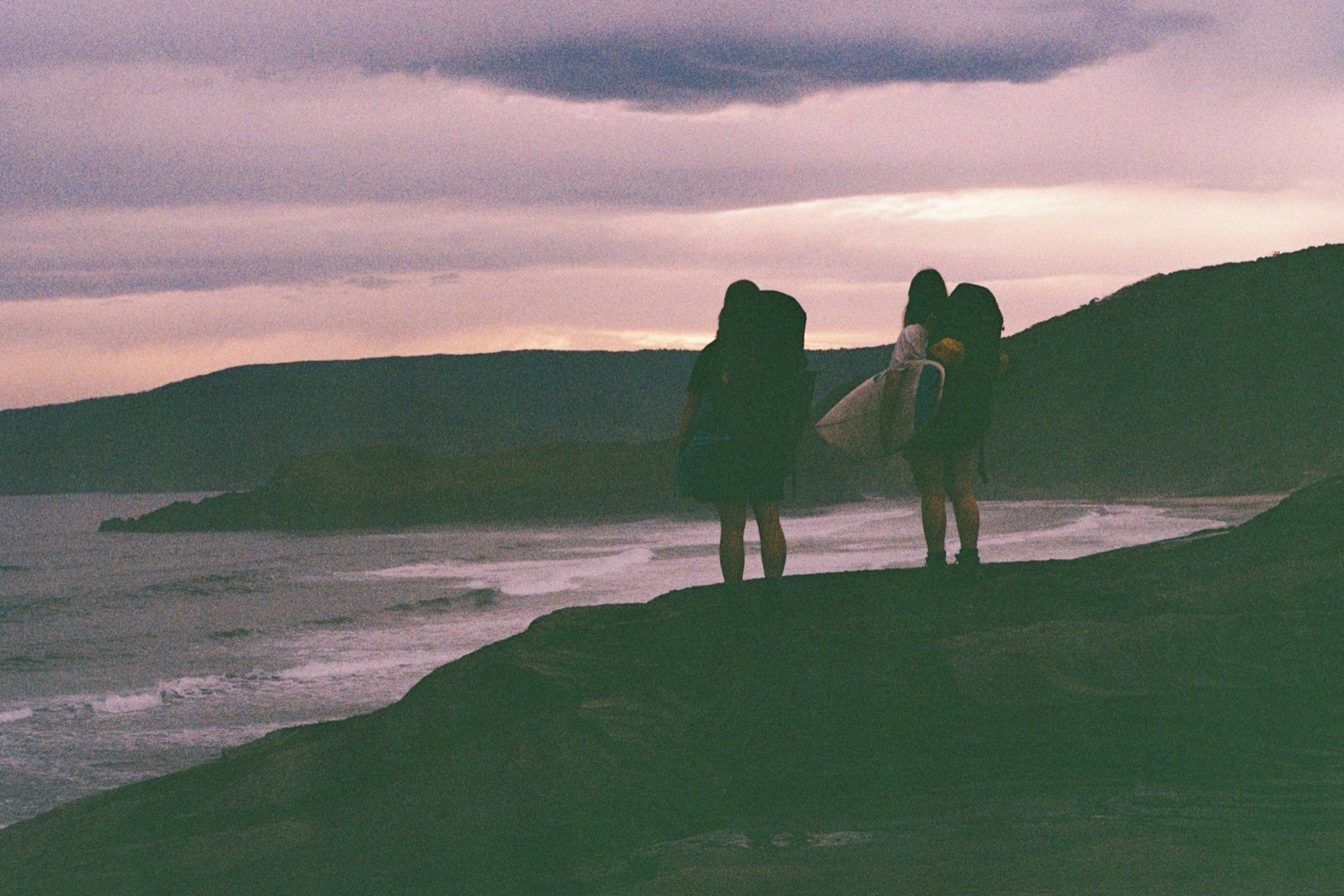 The three of us on a headland at dusk with boards and packs, looking down the point